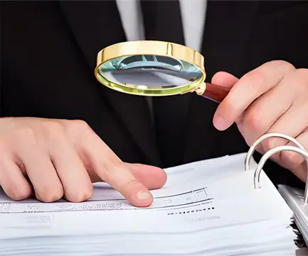 A person holding a magnifying glass over papers.